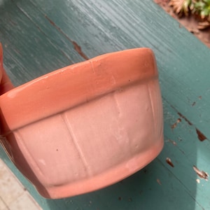 May include: A pink ceramic planter with a ribbed design. The planter is slightly chipped on the rim.