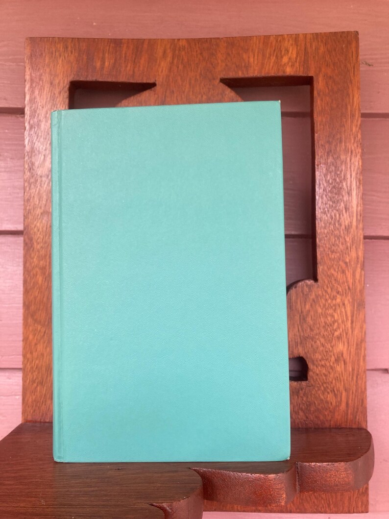 May include: A teal blue hardcover book with a smooth, textured cover. The book is sitting on a wooden shelf.