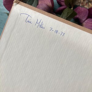 May include: A close-up of a book with a handwritten inscription that reads "Tina Mikus 7-18-77".