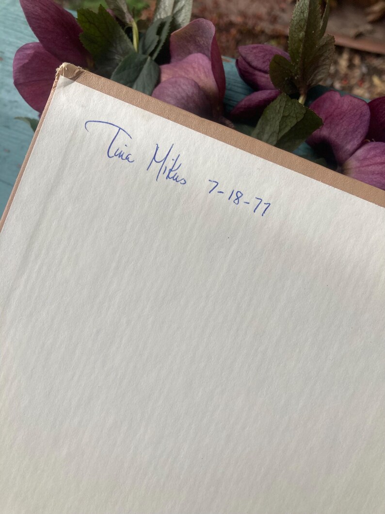 May include: A close-up of a book with a handwritten inscription that reads "Tina Mikus 7-18-77".