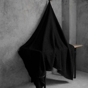 May include: A large, black, textured blanket draped over a small, dark metal table. The blanket is hanging from a wooden hook on a gray wall. The blanket's edges are slightly frayed.
