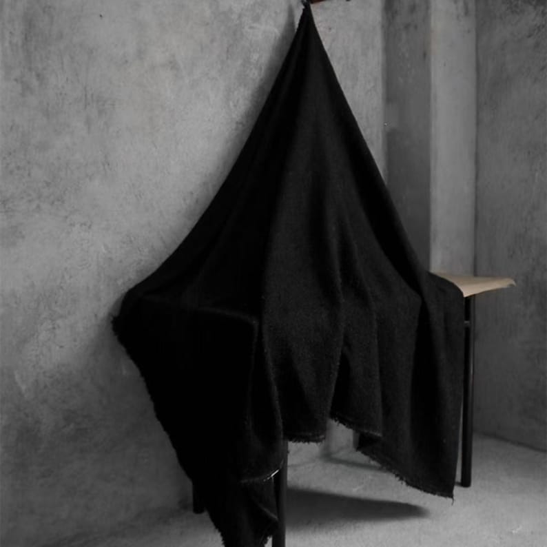 May include: A large, black, textured blanket draped over a small, dark metal table. The blanket is hanging from a wooden hook on a gray wall. The blanket's edges are slightly frayed.