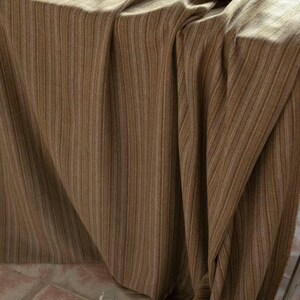 May include: A draped fabric with vertical stripes in shades of brown and tan. The material has a textured appearance, with subtle variations in color and a soft, flowing drape. The fabric is likely used for home decor or apparel.