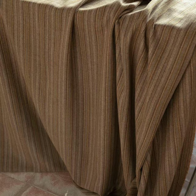 May include: A draped fabric with vertical stripes in shades of brown and tan. The material has a textured appearance, with subtle variations in color and a soft, flowing drape. The fabric is likely used for home decor or apparel.