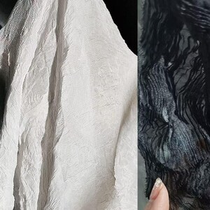 May include: Close-up of two fabrics, one white and one black. The white fabric has a textured, rippled surface. The black fabric has a similar texture, with a fringe-like appearance. The fabrics are likely textiles for clothing or home decor.