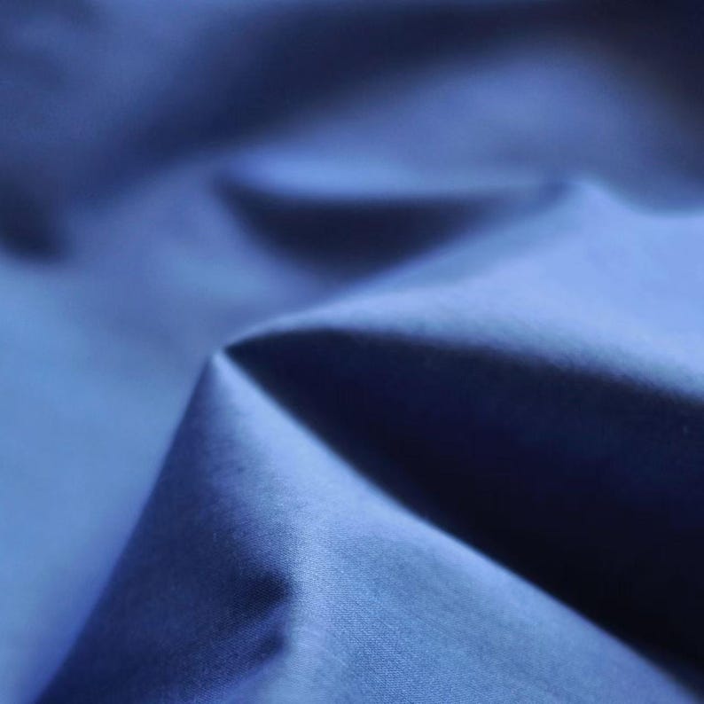 May include: Close-up of a folded piece of blue fabric. The fabric has a smooth, shiny texture and is a deep shade of blue. The folds create shadows and highlights, adding depth to the image. The fabric appears to be a luxurious material.