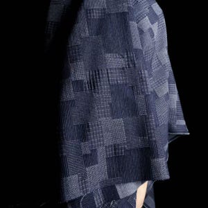 May include: A dark blue textile featuring a complex patchwork design of various geometric patterns, including fine vertical stripes, small squares, and grid textures, creating a dense, layered visual effect across the fabric surface.
