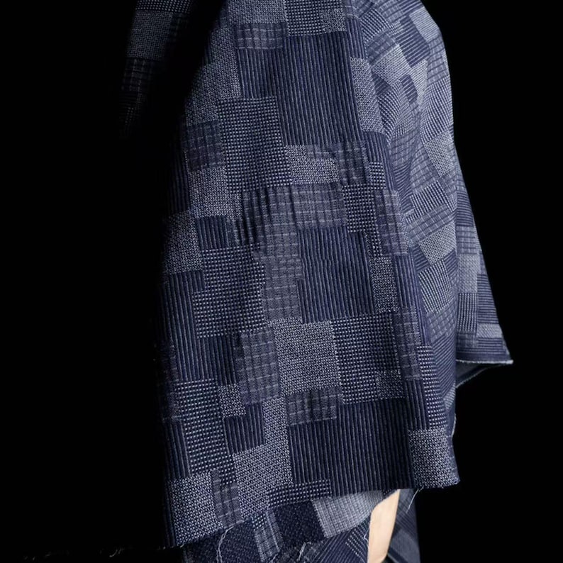 May include: A dark blue textile featuring a complex patchwork design of various geometric patterns, including fine vertical stripes, small squares, and grid textures, creating a dense, layered visual effect across the fabric surface.