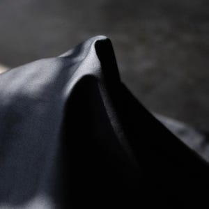 May include: Close-up of a dark, possibly black, fabric with a smooth, slightly reflective surface. The fabric is folded, creating a peak and shadows that add depth and texture. The lighting highlights the material's sheen.