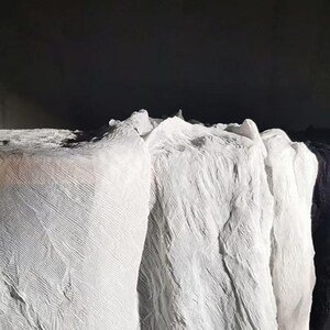 May include: Close-up of several rolls of white fabric with a textured, crinkled appearance. The fabric is arranged in a layered formation, with a dark background. The image highlights the texture and folds of the material.