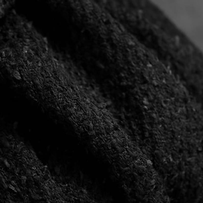 May include: Close-up of a textured, black fabric with visible folds and a slightly rough surface. The material appears to be thick and opaque, with subtle variations in tone, creating depth and shadow.