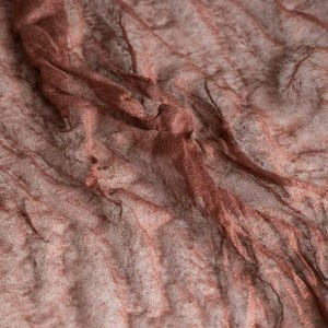 May include: Close-up of a sheer, textured fabric in shades of brown and reddish-brown. The material appears lightweight and slightly wrinkled, with subtle vertical stripes. The fabric's delicate weave is visible, creating a semi-transparent effect.