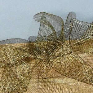 May include: Close-up of gold and black mesh fabric, possibly for decorative use. The mesh has a metallic sheen, with the gold sections appearing brighter than the black. The fabric is gathered and folded, creating a textured effect.