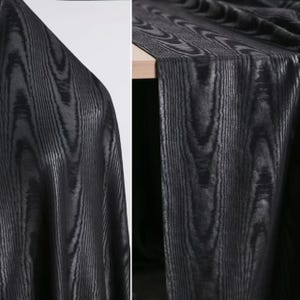 Puede incluir: Tela negra con un patr&oacute;n de vetas de madera. La tela est&aacute; drapeada de dos maneras diferentes, mostrando la textura y el dise&ntilde;o. El patr&oacute;n de vetas de madera es vertical y tiene un brillo met&aacute;lico.