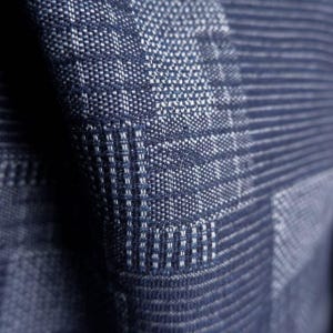 May include: A dark blue textile fabric featuring a woven pattern of alternating light and dark blue threads. The material displays a textured surface with a grid-like structure created by the interlacing of horizontal and vertical fibers.