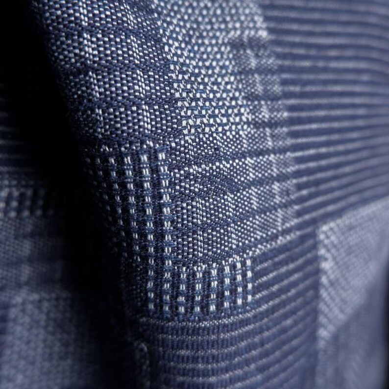 May include: A dark blue textile fabric featuring a woven pattern of alternating light and dark blue threads. The material displays a textured surface with a grid-like structure created by the interlacing of horizontal and vertical fibers.