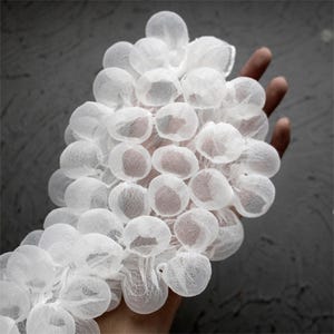 Peut inclure: Un ensemble d'objets blancs, ronds et translucides, possiblement décoratifs ou fonctionnels, tenus dans une main. Les objets ont une apparence délicate et aérienne, sur fond gris.