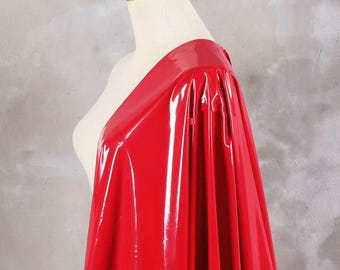 Puede incluir: Una tela roja brillante y brillante drapeada sobre un maniquí. El material tiene una superficie brillante y reflectante, que capta la luz. Una corona dorada se encuentra sobre la cabeza del maniquí, lo que sugiere un tema real. La textura de la tela es suave y parece ser sintética.
