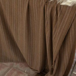 May include: Close-up of a brown fabric with vertical stripes. The fabric is draped, creating folds and shadows that add depth. The color is a warm, earthy tone, suitable for upholstery or drapery.