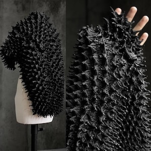 May include: A black, textured garment with a unique, spiky design. The garment is displayed on a mannequin and also shown in a close-up view, highlighting the intricate details of the fabric. The overall aesthetic is avant-garde and artistic.