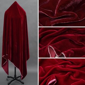 May include: A rich, deep red velvet fabric, possibly a shawl or cloak, is draped over a dress form. The fabric has a soft, lustrous appearance with a white trim. Close-up shots highlight the texture and folds of the material.