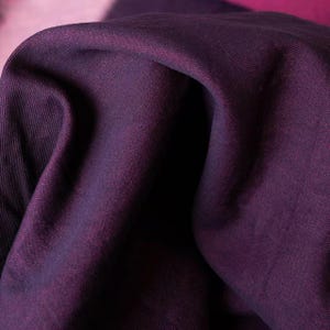Könnte beinhalten: Nahaufnahme eines tiefvioletten Stoffes mit sichtbarer Textur und Falten. Der Stoff hat einen subtilen Glanz, wobei dunklere Schatten Tiefe erzeugen. Die Farbe ist ein satter, gesättigter Farbton von Lila, geeignet für Kleidung oder Heimdekoration.