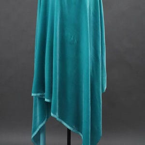 May include: A teal-colored, draped garment made of a soft, velvety fabric. The fabric hangs in graceful folds, with a layered design and a contrasting trim along the edges. The overall effect is elegant and flowing.