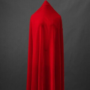 May include: A bright red fabric draped over a form, creating a flowing shape. The material appears soft with a slight sheen, with folds and shadows adding depth. The background is a solid, neutral grey.