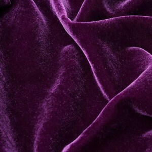 May include: A close-up shot of a deep purple velvet fabric, displaying soft folds and a luxurious sheen. The texture of the fabric is evident, emphasising its plushness and depth of colour. The image highlights the rich, saturated hue and how light interacts with the surface.