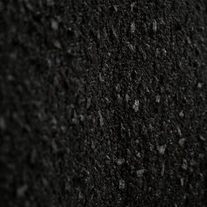 May include: Close-up of a black, textured fabric. The material has a dense, woven appearance with small, irregular bumps and a slightly uneven surface. The color is a deep, solid black.