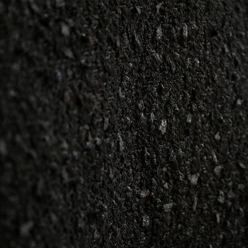 May include: Close-up of a black, textured fabric. The material has a dense, woven appearance with small, irregular bumps and a slightly uneven surface. The color is a deep, solid black.
