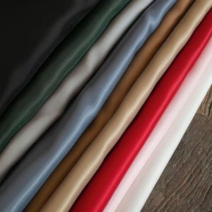 Könnte beinhalten: Eine Auswahl an farbigen Stoffmustern in verschiedenen Farbtönen, darunter Schwarz, Grün, Grau, Blau, Beige, Rot und Weiß. Die Stoffe sind diagonal angeordnet und zeigen ihre Texturen und Farben. Das Bild hebt die verschiedenen Materialien hervor.