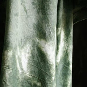 Puede incluir: Primer plano de una tela con un patr&oacute;n tie-dye en tonos verdes y blancos. La tela est&aacute; drapeada, mostrando pliegues y texturas. El patr&oacute;n de tinte crea un efecto marmolado, con &aacute;reas de verde m&aacute;s claro y oscuro.