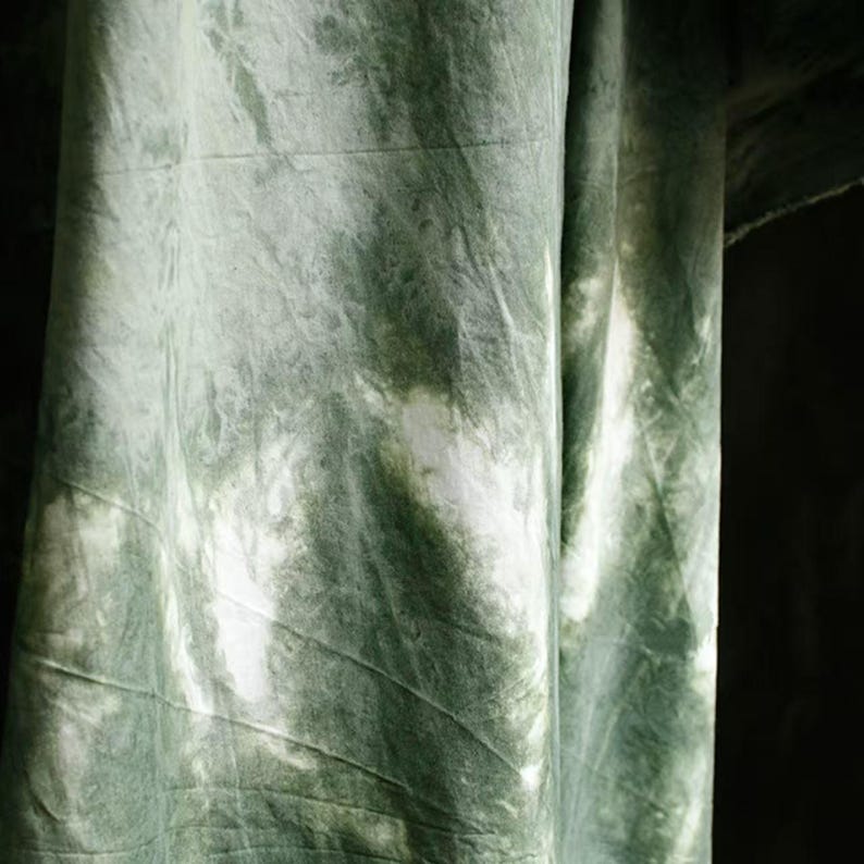 Puede incluir: Primer plano de una tela con un patr&oacute;n tie-dye en tonos verdes y blancos. La tela est&aacute; drapeada, mostrando pliegues y texturas. El patr&oacute;n de tinte crea un efecto marmolado, con &aacute;reas de verde m&aacute;s claro y oscuro.