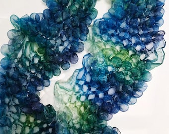 Puede incluir: Primer plano de una bufanda decorativa en tonos azules y verdes. La bufanda tiene un diseño texturizado único con una apariencia burbujeante y en capas. Los colores se mezclan desde azules profundos hasta verdes más claros, creando un efecto degradado.