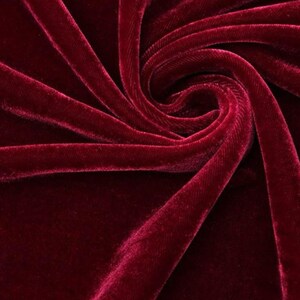 May include: Close-up of a deep red velvet fabric with a soft, luxurious texture. The fabric is arranged in swirling folds, creating shadows and highlights that emphasise its plushness. The rich colour and tactile quality suggest a high-end textile.