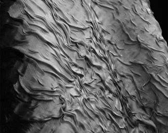 May include: A close-up, grayscale image of a textured surface with a rippled, flowing appearance. The surface has a fabric-like quality, with deep folds and shadows creating a sense of depth and movement. The overall effect is abstract and artistic.