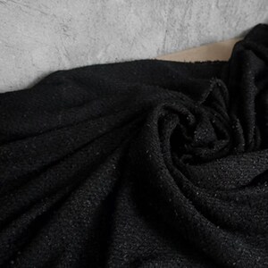 May include: A close-up shot of a dark, textured fabric with a woven appearance. The fabric is a deep black color, with subtle variations in tone and texture. The material is draped and folded, creating shadows and highlights.
