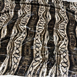 May include: Close-up of a fabric with a snakeskin pattern. The fabric has vertical stripes in shades of brown, tan, and black, creating a textured and detailed design. The pattern mimics the scales and markings of a snake.