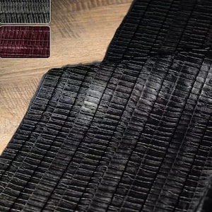Könnte beinhalten: Nahaufnahme eines strukturierten schwarzen Stoffes mit einem gitterartigen Muster. Der Stoff scheint Leder oder ein lederähnliches Material zu sein. Zwei kleinere Stoffmuster befinden sich in der oberen linken Ecke, eines grau und eines weinrot.