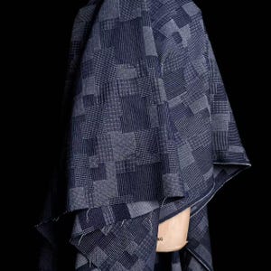 May include: A dark blue fabric featuring a patchwork design of various geometric patterns including stripes, grids, and small dots. The textile is draped over a light-colored mannequin form, showcasing the intricate woven textures and deep indigo tones.