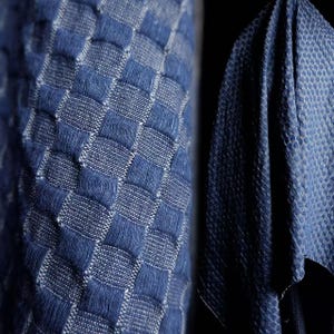 Könnte beinhalten: Ein Textilstoff mit einem tiefblauen und weißen gewebten Schachbrettmuster und einer erhabenen, strukturierten Oberfläche. Das Material zeigt eine dichte, gitterartige Struktur mit abwechselnden Quadraten aus blauen und weißen Fäden.