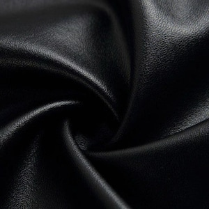 May include: Close-up of black leather fabric with a textured surface. The leather is folded and draped, creating shadows and highlights that emphasize its supple quality. The image showcases the material's rich color and subtle sheen.