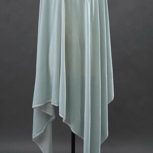 May include: A flowing, light blue fabric with a draped design. The fabric has a soft, velvety texture and is likely used for clothing or decorative purposes. The edges are finished with a contrasting white trim.