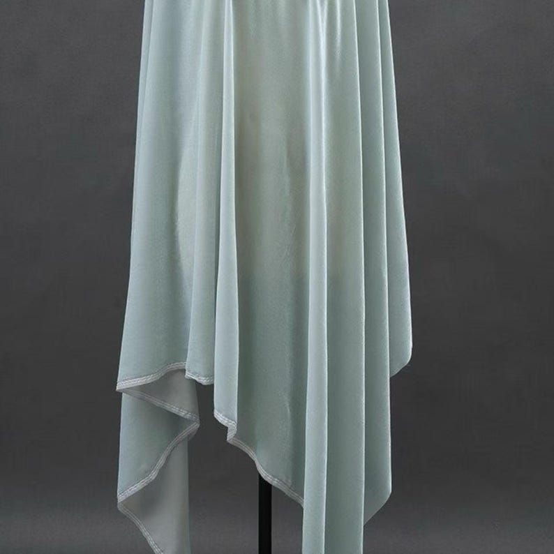 May include: A flowing, light blue fabric with a draped design. The fabric has a soft, velvety texture and is likely used for clothing or decorative purposes. The edges are finished with a contrasting white trim.