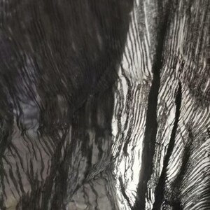 May include: Abstract image of a dark, textured fabric with a rippled effect. The fabric appears to be black or a very dark color, with areas of light and shadow creating a sense of depth and movement. The texture has a striped pattern.