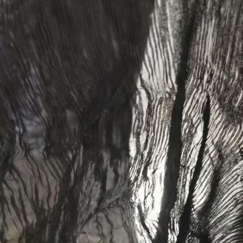 May include: Abstract image of a dark, textured fabric with a rippled effect. The fabric appears to be black or a very dark color, with areas of light and shadow creating a sense of depth and movement. The texture has a striped pattern.