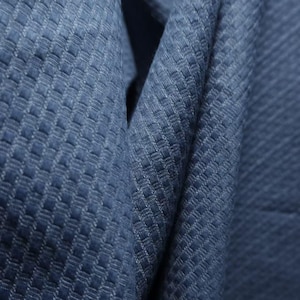 May include: A deep blue fabric featuring a distinct, raised grid-like texture. The material is folded, creating soft shadows and highlights that emphasize the repeating square pattern woven into the surface of the textile, showcasing its depth.