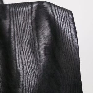 Puede incluir: Una tela negra con una textura vertical distintiva que recuerda a la veta de la madera. El material presenta un brillo sutil que resalta los patrones lineales en relieve en toda la superficie, creando un aspecto monocrom&aacute;tico y texturizado.