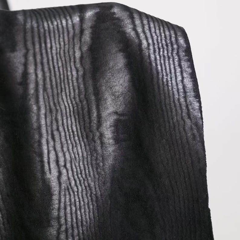 Puede incluir: Una tela negra con una textura vertical distintiva que recuerda a la veta de la madera. El material presenta un brillo sutil que resalta los patrones lineales en relieve en toda la superficie, creando un aspecto monocrom&aacute;tico y texturizado.